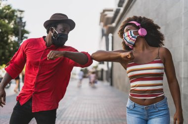 Yüz koruma maskesi takan Afrikalı arkadaşlar yeni sosyal uzaklık kutlamaları yaparken dirseklerini çarpıştırıyorlar - Gençlik çağındaki insanlar ve Corona virüsünün yayılmasını önlemek için sağlık kılavuzları