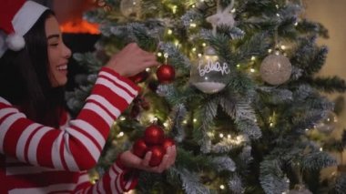 Mutlu genç bir kadın Noel ağacını süslerken eğleniyor.