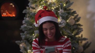 Mutlu genç kız Noel tatilini kutlarken cep telefonu kullanıyor.