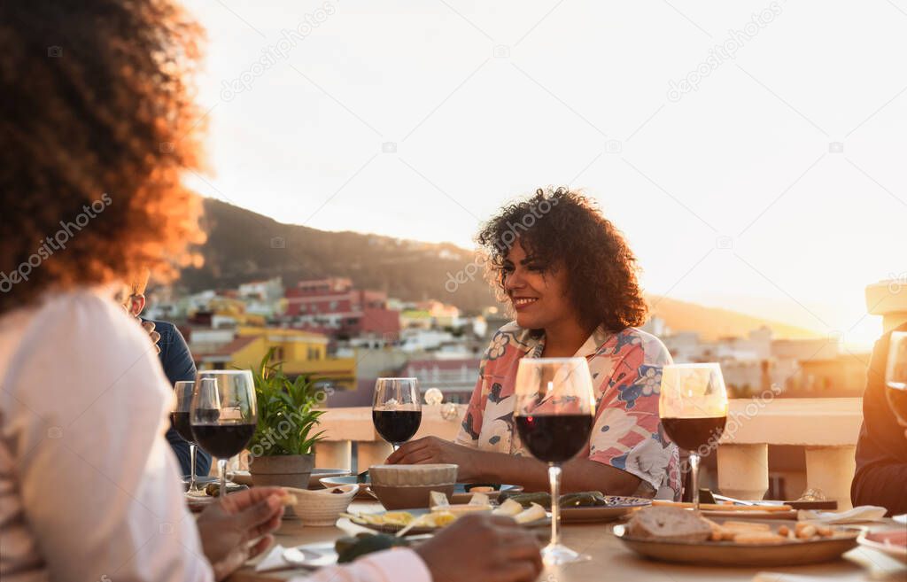 Young multiracial friends doing appetizer and drinking red wine on house patio during sunset time