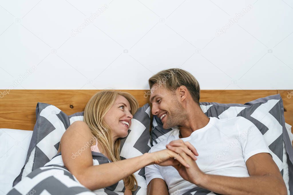 Happy smiling couple lying on bed having tender moments - Young people love and relationship concept