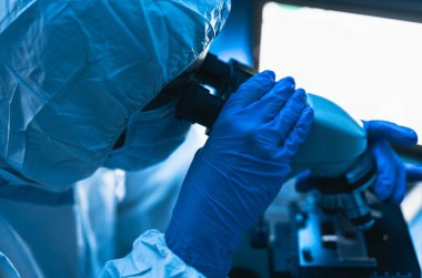 Laboratuvarda çalışan genç bilim adamı mikroskopla Coronavirus 'u inceliyor. Bilim ve teknoloji kavramı.