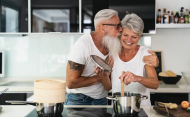 Mutlu son sınıf çifti evde birlikte yemek pişirirken eğleniyor - yaşlı insanlar modern mutfakta öğle yemeği hazırlarken - emekli yaşam tarzı aile zamanı ve gıda beslenme konsepti