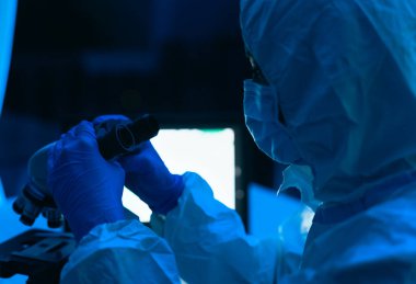 Laboratuvarda çalışan genç bilim adamı mikroskopla Coronavirus 'u inceliyor. Bilim ve teknoloji kavramı.