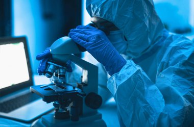 Laboratuvarda çalışan genç bilim adamı mikroskopla Coronavirus 'u inceliyor. Bilim ve teknoloji kavramı.