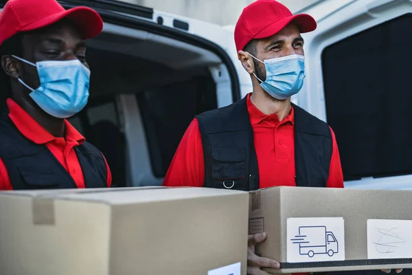 Young delivery men carrying cardboard box while wearing face mask to avoid corona virus spread - People working with fast deliver during corona virus outbreak