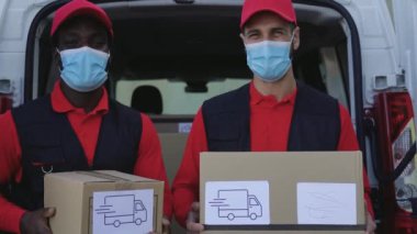 Corona virüsünün yayılmasını önlemek için yüz maskesi takmış karton kutu taşıyan genç teslimatçılar Corona virüsü salgını sırasında hızlı bir şekilde teslim ediliyor.