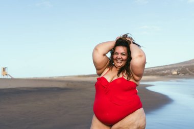 Plajda poz veren mutlu, kilolu bir kadın, aşırı kilolu bir model, tropikal bir yerde tatil yaparken eğleniyor.