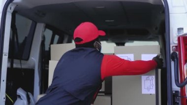 Corona virüsünün yayılmasını önlemek için yüz maskesi takan Afrikalı kurye kamyonete kutu yüklüyor.
