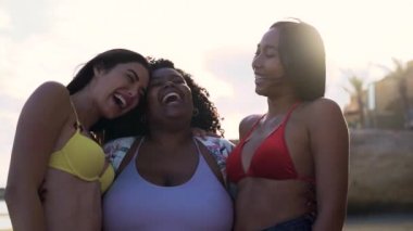 Farklı vücut ölçülerine sahip mutlu çok ırklı kadınlar yaz tatillerinde sahilde eğleniyorlar.