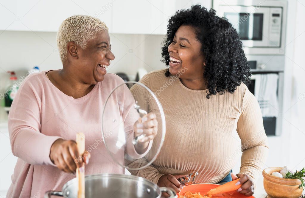 Happy Afro mother and daughter preparing lunch together in modern house kitchen - Food and parents unity concept
