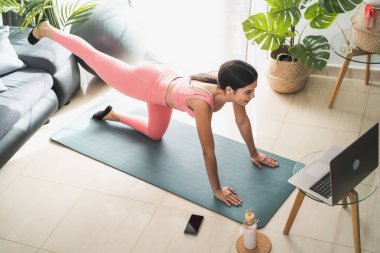 Genç Latin bir kadın evde bilgisayarlı pilates sanal fitness dersi alıyor. Spor sağlığı, yaşam tarzı kavramı.