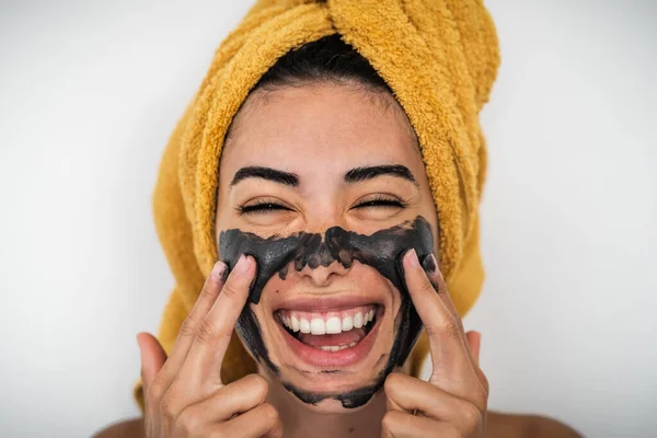 Young smiling woman applying charcoal mask on face - Happy girl having skin care spa day at home - Healthy beauty clean treatment and youth people lifestyle concept