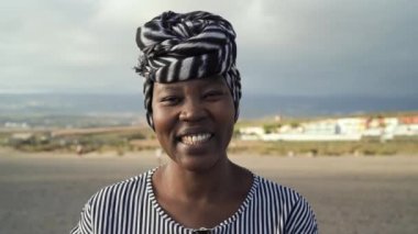 Mutlu Müslüman Afrikalı kadın yaz tatilinde kumsalda kameraya gülümsüyor.