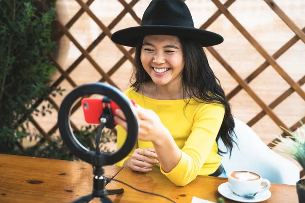 快乐的亚洲女人坐在酒吧里喝咖啡时 用智能手机摄像头和有影响力的人在网上大吵大闹 — 图库照片