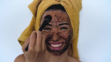 Gülümseyen ve yüzünde fırçayla maske takan genç bir kadın - Mutlu kız evde cilt bakımı spası yaptırıyor - sağlıklı alternatif deri yüzme tedavisi ve gençlerin yaşam tarzı kavramı
