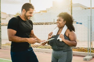 Personal trainer working with curvy woman while giving her istruction with digital tablet during training session - Sport people lifestyle concept clipart