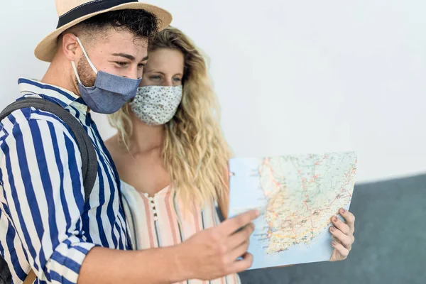 旅行若いカップルは コロナウイルスを防ぐためにフェイスマスクを身に着けている間旅行中に都市マップを保持 — ストック写真