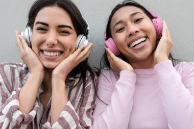 Genç mutlu Latin kızlar dışarıda kablosuz kulaklıklarla müzik dinleyerek eğleniyorlar.