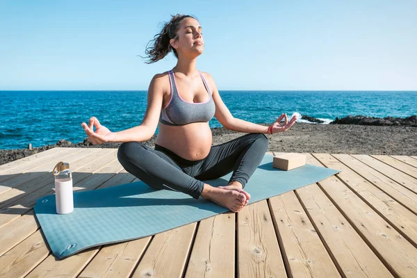 海の隣でヨガセッションを行う若い妊婦 瞑想と妊産婦の概念 — ストック写真