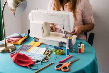 Dikiş makinesiyle çalışan kadın Corona virüsünün yayılmasını önlemek ve durdurmak için ev yapımı yüz maskesi yapıyor. Tekstil terzisi ve ev yapımı insanlar konsepti.