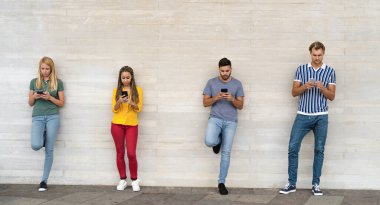 Genç, çok ırklı bir arkadaş grubu açık havada cep telefonu kullanıyor. Gençlik çağındaki yaşam tarzı kavramı.