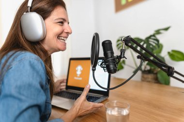 Olgun bir kadın, stüdyosundaki mikrofon ve dizüstü bilgisayarla podcast yapıyor.