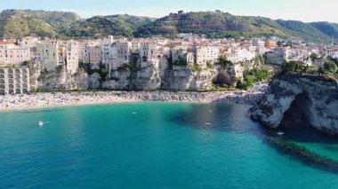 Hava manzarasında Tropea 'nın turkuvaz suları, kalabalık bir kumlu plaj ve dramatik uçurumların tepesine tünemiş binalar yer alıyor. Calabria 'daki büyüleyici İtalyan tatil köyü görünüyor..