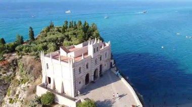 Açık mavi denizle çevrili kayalık bir adada Santa Maria dell 'Isola tapınağını görüntüler. Uzaklardan küçük tekneler görünüyor..