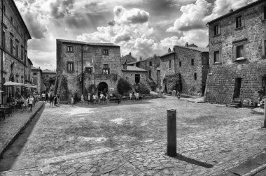 CIVITA DI BAGNOREGIO, İtalya - 15 Ağustos 2025: Civita di Bagnoregio tarihi taş binalar ve canlı turist kalabalığını barındırıyor. Güneşli gökyüzü dramatik beyaz bulutlarla doludur.