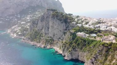 Bir hava manzarası, İtalya 'nın Capri kentindeki engebeli uçurumları ve yemyeşil tepeleri parlak bir gökyüzünün altında beyaz binalarla süslüyor..
