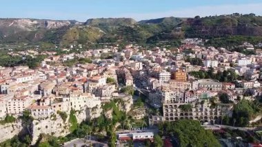 Havadan geniş bir görüntü, yoğun şehir merkeziyle dramatik sahil uçurumlarının tepesine tünemiş Tropea, İtalya 'yı gözler önüne seriyor. yemyeşil tepeler ve dağlar manzaralı bir zemin oluşturur..