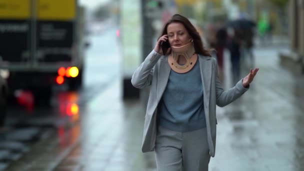 Middle-aged businesswoman with cervical collar is walking on street and talking by mobile phone — Stock Footage Middle-aged businesswoman with cervical collar is walking on street and talking by mobile phone Stock Footage