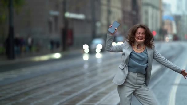 Funny woman with neck brace is dancing cheerfully on tram stop in city, fun and joke — Stock Footage Funny woman with neck brace is dancing cheerfully on tram stop in city, fun and joke Stock Video