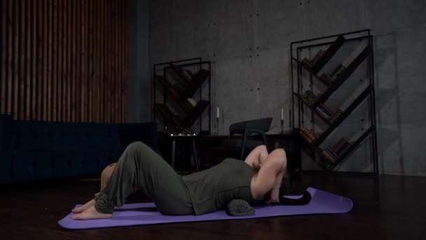 Woman is healing pain in back, lying on floor with roller under spine, exercise for stretching muscles — Stock Footage Woman is healing pain in back, lying on floor with roller under spine, exercise for stretching muscles Video Clip