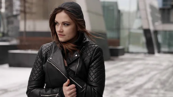 young brunette lady is walking alone in city at cold winter day, wrapping in leather jacket