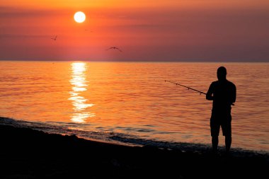 Kumsalda bir balıkçının siluetiyle Karadeniz 'in üzerinde gün doğumu. Denizde sabah balıkçılığı.