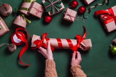 Yeşil arka planda kırmızı kurdeleli hediye kutusunu saran kadın eller. Tatil hazırlığı. Noel, kış, yeni yıl konsepti. Düz konum, üst görünüm, kopyalama alanı.
