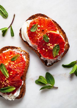 Mermer kesim tahtasının üzerinde krem peynirli ve naneli turuncu tost. Kapat..