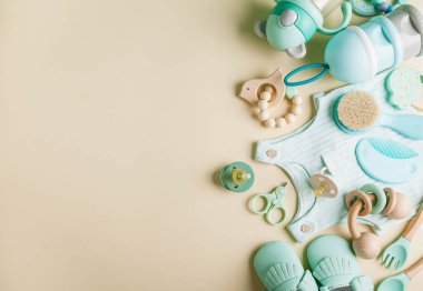 Bebek bakım aksesuarları, giysiler ve botlar. Yeni doğmuş bebek emziği, bağcıklar, tırnak makası, saç fırçası, bej arka planda kaşık ve çatal. Hamilelik için dilek listesi ya da alışveriş özeti. Düz yatış, üst görünüm.