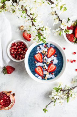 Kelebek bezelyeli chia pudingi çilek, nar ve granola beyaz arka planda beyaz bir kasede. Süper yiyecek ve vejetaryen konsepti. Mavi kibrit tozu.