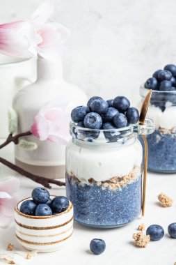 Beyaz arka planda cam kavanozlarda yabanmersinli bezelye çiçeği parfe. Mavi kiraz chia pudingi. Süper yiyecek ve vegan konsepti.  