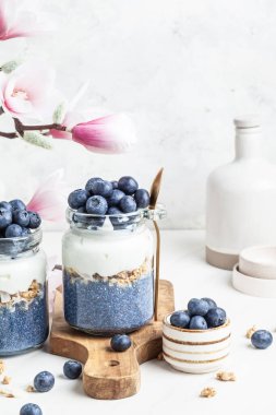 Beyaz arka planda cam kavanozlarda yabanmersinli bezelye çiçeği parfe. Mavi kiraz chia pudingi. Süper yiyecek ve vegan konsepti.  