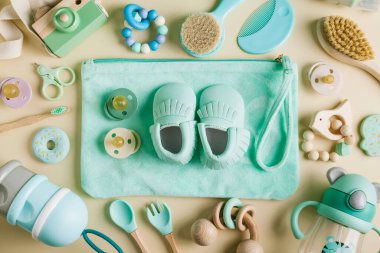 Bebek bakım aksesuarları ve botlar. Yeni doğmuş bebek emziği, bağcıklar, tırnak makası, saç fırçası, bej arka planda kaşık ve çatal. Hamilelik için istek listesi veya alışveriş genel görünümü. 