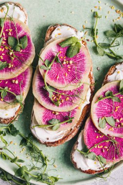 Krem peynirli karpuzlu turp tostu ve yeşil seramik tabakta mikro-yeşil bezelye. Sağlıklı beslenme kavramı. Düz yatış, üst görünüm.