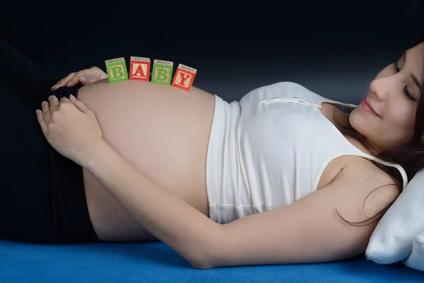 Pregnant asian woman put a wooden letter "BABY" on her belly whi — Stock Photo, Image