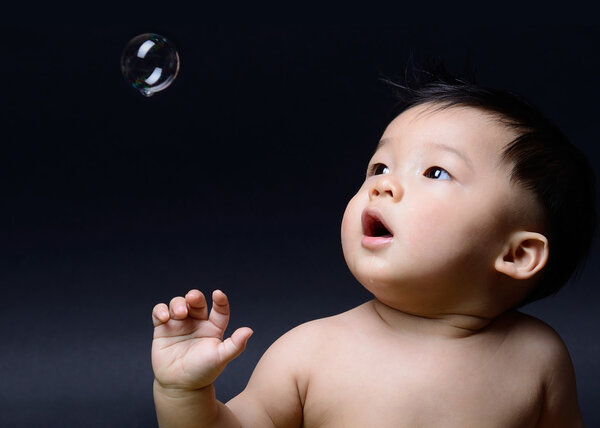 little baby asian boy drooling and looking soap bubble
