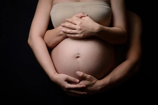 Руки вагітної жінки і її чоловіка на животі — стокове фото