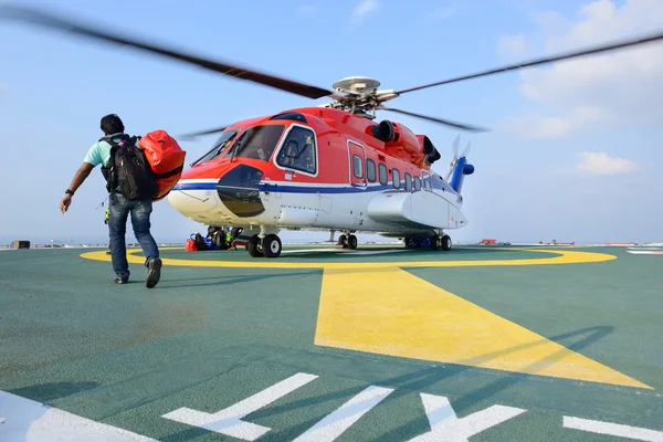 Matkustaja kuljettaa matkatavaransa noustakseen helikopteriin öljynporauslautalla — kuvapankkivalokuva
