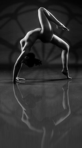 Flexibility and beauty. Beautiful sexy body of young woman on black background. Low key black and white studio photography. Amazing yoga poses with reflections